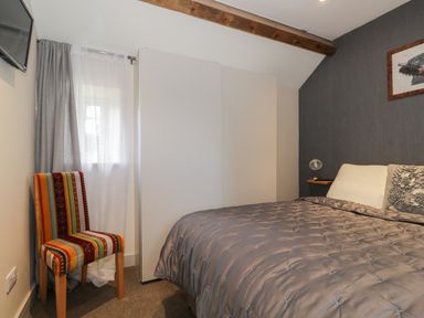 A bedroom with a patterned chair next to a window and a bed with a gray comforter at The Granary Loft in Bardsea