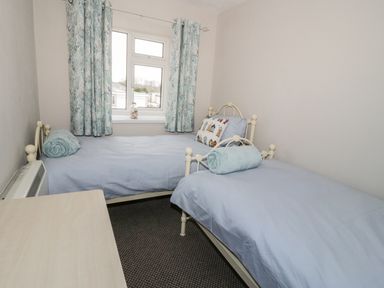 A bedroom with two single beds a window with curtains and a desk at Harbour View in Cemaes Bay