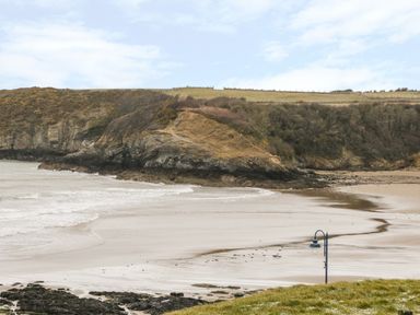 A sandy beach with waves and rocky cliffs in the background at Harbour View in Cemaes Bay