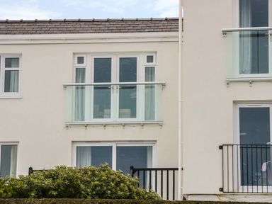 A building facade with glass balconies and windows above bushes at Harbour View in Cemaes Bay
