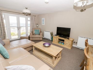 A living room with leather sofas a wooden coffee table a television and glass doors overlooking the sea at Harbour View in Cemaes Bay