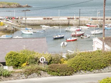 A harbor with boats on the water and a stone wall with bushes in the foreground at Harbour View in Cemaes Bay