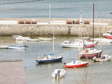 A harbor with several small boats and sailboats moored near a stone wall with benches at Harbour View in Cemaes Bay