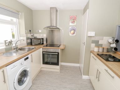 A kitchen with washing machine oven stovetop microwave and canisters at Harbour View in Cemaes Bay
