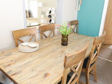 A wooden dining table with wooden chairs a vase with flowers and stacked plates in a dining room at Harbour View in Cemaes Bay