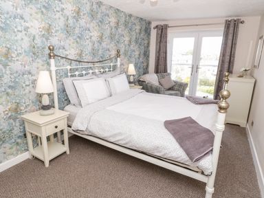 A bedroom with a bed two bedside tables with lamps an armchair and glass doors with curtains at Harbour View in Cemaes Bay