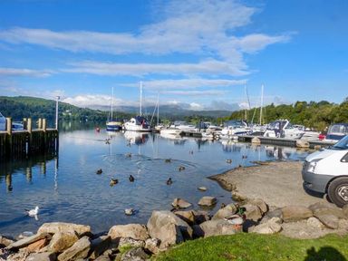 A marina with boats docked on the water and ducks swimming near rocks and a vehicle at Coniston Number 9 in White Cross Bay
