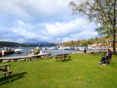 A grassy area with picnic benches a wooden dock with boats on the water and trees at Coniston Number 9 White Cross Bay