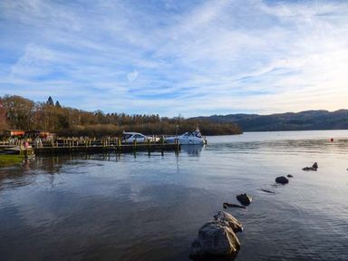 A lake with boats docked at a wooden pier and hills in the background at Coniston Number 9 White Cross Bay