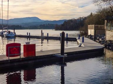 A dock with boats on a lake surrounded by trees and hills at Coniston Number 9 in White Cross Bay