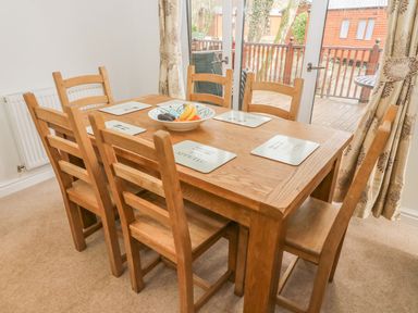 A dining room with a wooden table and six chairs a bowl of fruit on the table and glass doors leading to a wooden deck at Coniston Number 9 in White Cross Bay
