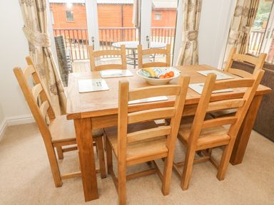 A dining area with a wooden table and six chairs a bowl of fruit on the table and sliding glass doors with curtains at Coniston Number 9 in White Cross Bay