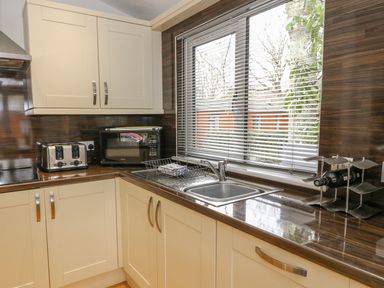 A kitchen corner with a sink, toaster, microwave, and wine rack by a window at Coniston Number 9 in White Cross Bay
