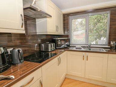 A kitchen with cream cabinets a stovetop toaster kettle microwave and a window with blinds at Coniston Number 9 in White Cross Bay