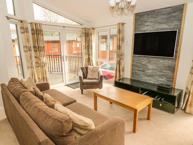 A living room with sofa armchair coffee table television and large windows at Coniston Number 9 in White Cross Bay