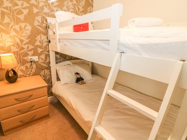 A bedroom with white bunk beds a wooden chest of drawers a lamp and wallpaper at Coniston Number 9 in White Cross Bay