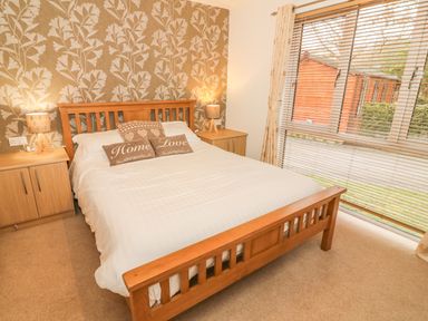 A bedroom with a wooden bed and white bedding two bedside tables with lamps and a window with blinds at Coniston Number 9 in White Cross Bay