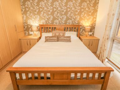A bedroom with a wooden bed frame white bedding two bedside tables with lamps built-in wooden wardrobes and a window with blinds and curtains at Coniston Number 9 in White Cross Bay