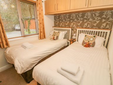 A bedroom with two single beds with owl cushions and folded towels by a window at Coniston Number 9 in White Cross Bay