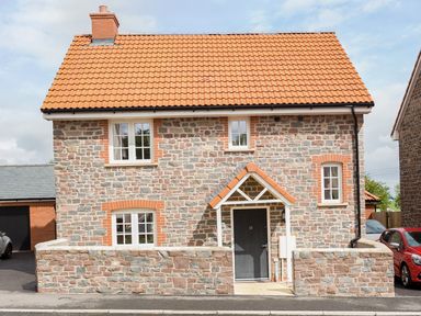 A stone house with a tiled roof and a black door with porch at Tus Nua Cottage in Carhampton
