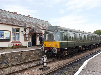 A green vintage train at a small station platform with a building marked booking office at Tus Nua Cottage in Carhampton
