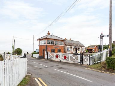 A railway crossing with closed gates near a small brick signal box and buildings by the sea at Tus Nua Cottage in Carhampton