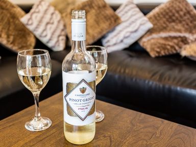 A bottle of white wine and two glasses on a wooden table in front of a couch with cushions at Tus Nua Cottage in Carhampton