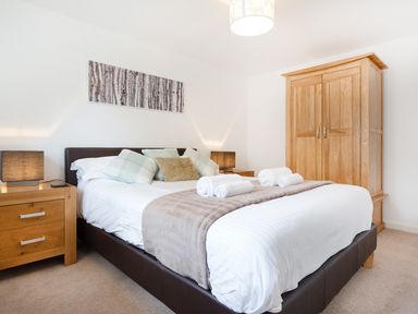 A bedroom with a bed cushions bedside tables lamps wardrobe and a framed picture at Tus Nua Cottage in Carhampton