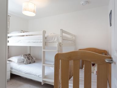 A bedroom with white bunk beds and a wooden crib with teddy bears at Tus Nua Cottage in Carhampton