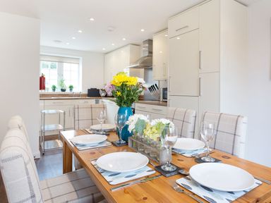 A dining table set with plates and glasses in a kitchen with cabinets and a window at Tus Nua Cottage in Carhampton