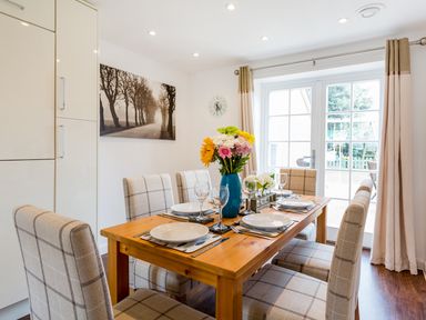 A dining room with a wooden table set for six with plates and glasses and a vase of flowers at Tus Nua Cottage in Carhampton