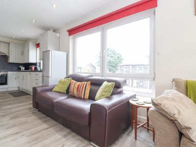 A living room with a brown leather sofa with cushions next to a window and kitchen cabinets visible in the background at Jakanori in Staveley