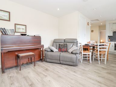 A living room with a piano a gray sofa and a dining table with chairs at Jakanori Staveley