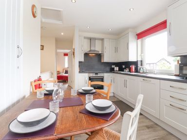 A kitchen with wooden dining table set with bowls and plates next to white cabinets and a window with a red blind at Jakanori in Staveley