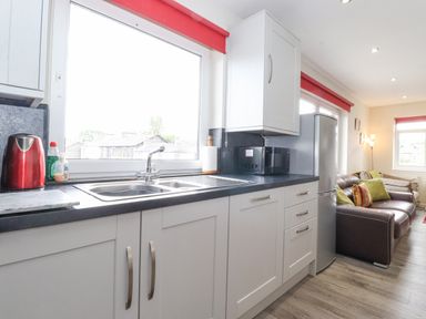 A kitchen with white cabinets a double sink a microwave a refrigerator and living area with brown sofa and pillows at Jakanori in Staveley