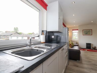 A kitchen sink with a faucet and paper towel holder next to a microwave and refrigerator in a room with a sofa and framed picture at Jakanori in Staveley