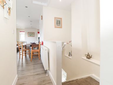 A hallway leading to a dining area with wooden chairs and a table a staircase with a teapot on a shelf on the side at Jakanori in Staveley