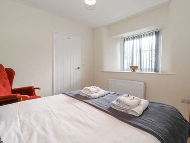 A bedroom with a bed, folded towels, an armchair, a window with vertical blinds, and a closed door at Jakanori in Staveley