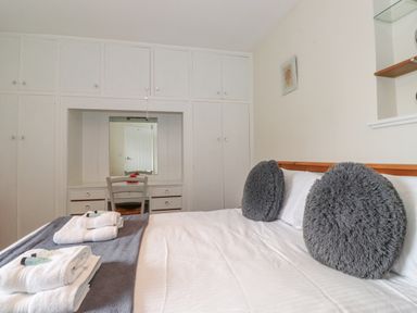 A bedroom with a bed with grey round cushions and folded towels on it with white wardrobes and a small desk with a chair and mirror at Jakanori in Staveley