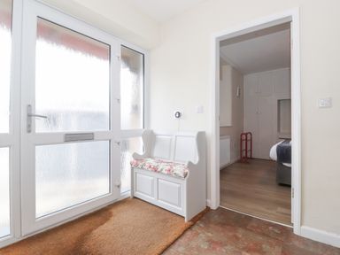 An entrance area with a white bench with floral cushion and a door leading to a bedroom with white wardrobes at Jakanori in Staveley