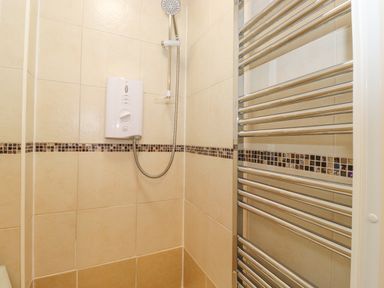 A shower area with a wall-mounted shower unit and a metal towel radiator in a tiled bathroom at Jakanori in Staveley