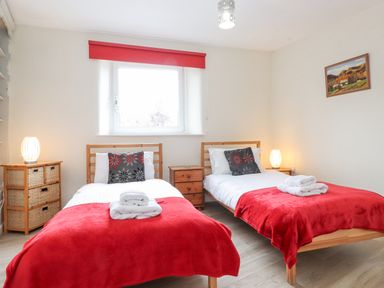 A bedroom with two single beds with red blankets and floral pillows two side tables with lamps and a window with a red blind at Jakanori in Staveley