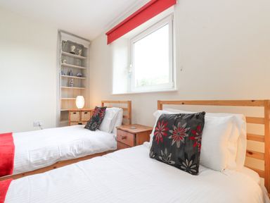 A bedroom with two single beds cushions and red throws a window a bedside table a small chest of drawers a lamp and shelves with decorative items at Jakanori Staveley