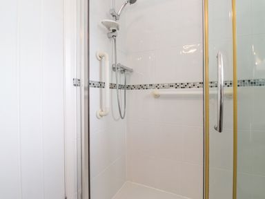 A shower area with white tiles grab bars a handheld showerhead and a glass door at Jakanori in Staveley
