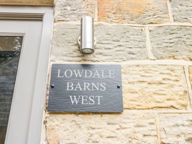 A stone wall with a gray plaque reading lowdale barns west and a silver outdoor light above it at Lowdale Barns West in Sleights