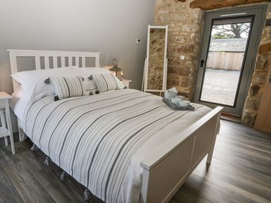 A bedroom with a white bed and striped bedding a floor mirror and a glass door showing an outside area at Lowdale Barns West in Sleights