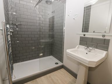 A bathroom with a walk in shower with gray tiles and a white pedestal sink at Lowdale Barns West in Sleights