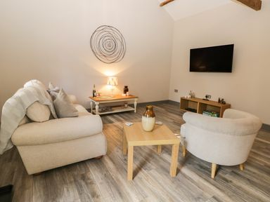 A living room with two beige sofas a wooden coffee table with a vase a wall-mounted TV and a small side table with a lamp at Lowdale Barns West in Sleights