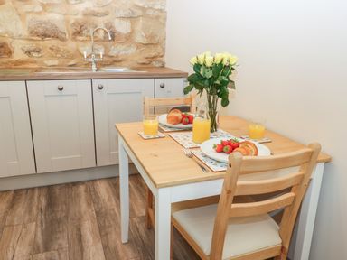 A small kitchen dining area with a wooden table set with croissants strawberries orange juice and a vase of yellow roses at Lowdale Barns West in Sleights
