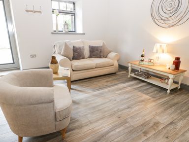 A living room with a beige sofa and armchair wooden coffee table lamp and decorative items at Lowdale Barns West in Sleights